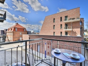 Ein Balkon mit Tisch und Stühlen, im Hintergrund ein Backsteinhaus und ein klarer Himmel.