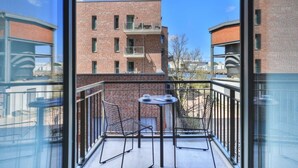 A balcony with a table and chairs, overlooking a brick building with multiple windows and balconies.