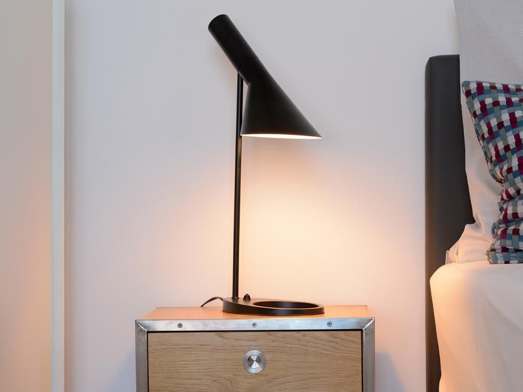 Ein Nachttisch mit einer schwarzen Schreibtischlampe, einer Schublade und einem kleinen runden Gegenstand darauf.