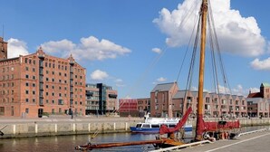 A waterfront area with a tall mast structure, a docked boat, and buildings in the background.