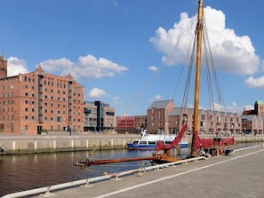 A waterfront area with a tall mast structure, a docked boat, and buildings in the background.