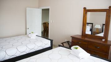 Habitación de hotel con dos camas, un aparador de madera, un espejo y una puerta que da a otra habitación.