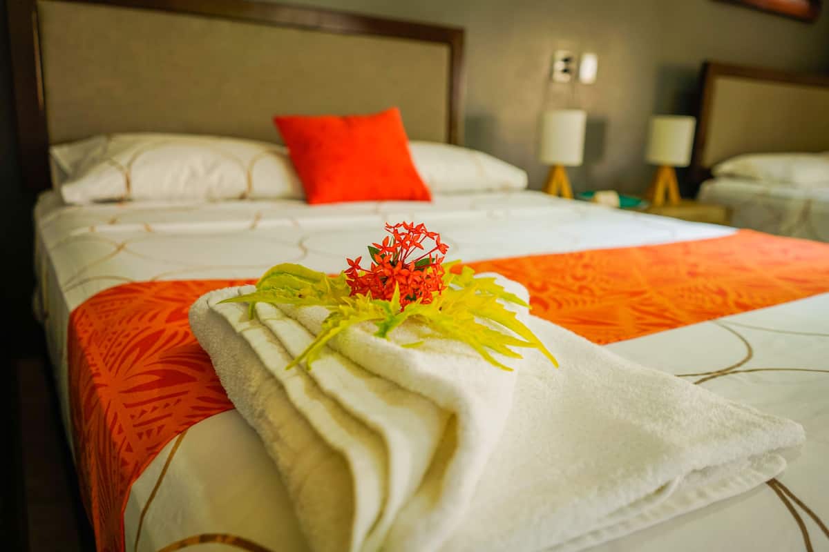 A neatly made bed with a white and orange bedspread, a red pillow, and a decorative floral arrangement on the bed.