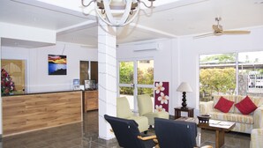 Amplia sala de estar con un mostrador de recepción de madera, un área de descanso y ventanas amplias que ofrecen vistas al exterior.