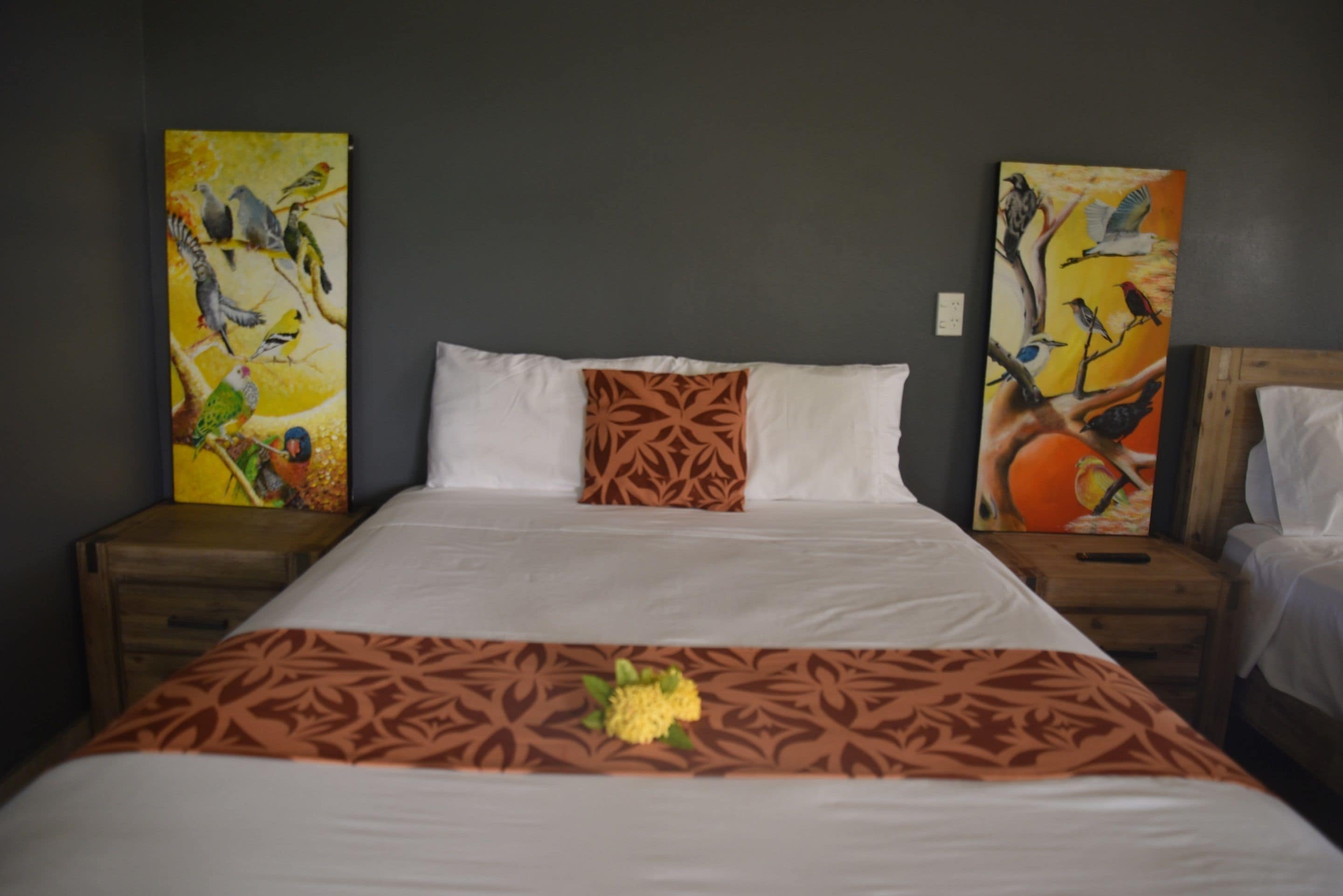 A hotel room with a large bed, two paintings on the walls, and a nightstand with a lamp.