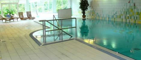 Una piscina interior con suelo de baldosas, barrera de cristal y una planta en maceta.