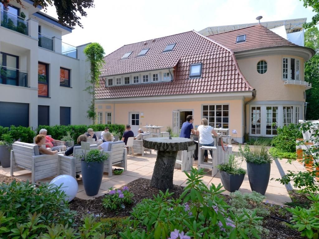 Ein Innenhof mit Außenbestuhlung, einem zentralen Baum und einem Gebäude mit Ziegeldach.