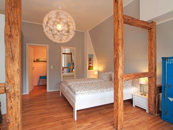 A bedroom with a wooden ceiling, a bed with a floral bedspread, a bedside table with a lamp, and a blue wardrobe.