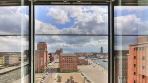 A view from a high-rise window overlooking a riverside promenade with buildings and a playground.