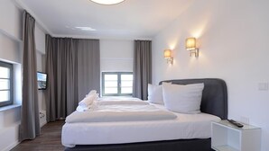 A modern hotel room with a large bed, a bedside table, a TV, and a window with curtains.