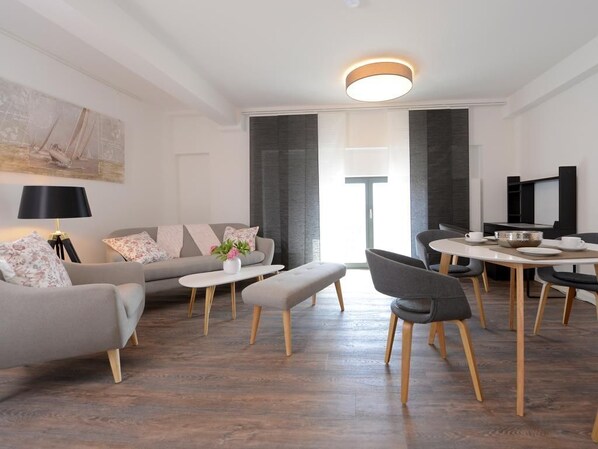 A modern living room with a sofa, a dining table, and a TV. - Ohlerich storage app. 36 - Ohlerich Speicher App. 36 (Wismar)