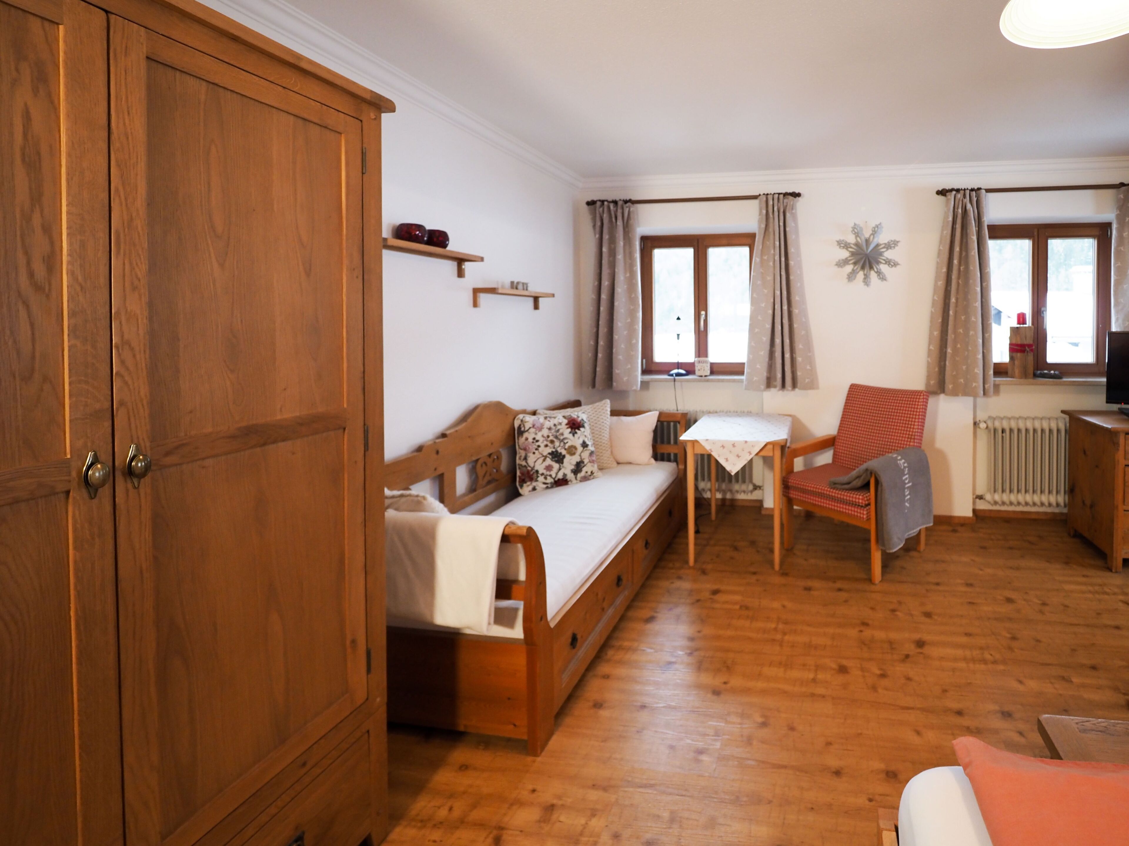 Una habitación acogedora con un armario de madera, una cama con un cojín estampado, una mesita, una silla y un radiador.