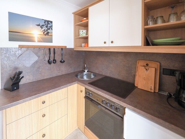 Een keuken met een fornuis, spoelbak, houten kastjes en een rek met keukengerei.