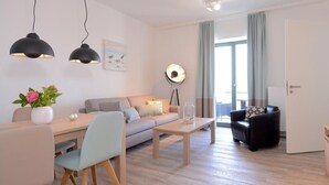 Ein modernes Wohnzimmer mit Sofa, Couchtisch und Essbereich. Eine Lampe, eine Vase mit Blumen und ein Gemälde sind an der Wand zu sehen.