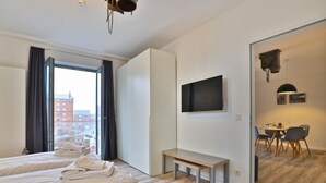 Une chambre d’hôtel avec deux lits, une télévision, un banc, un coin repas et une vue sur les bâtiments environnants.
