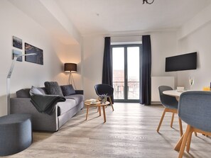 Een moderne woonkamer met een bank, een salontafel, een televisie en uitzicht op een balkon.