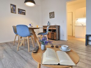 Une pièce comprenant une table à manger, des chaises, une télécommande, un livre ouvert, un vase avec des fleurs et une horloge au mur.