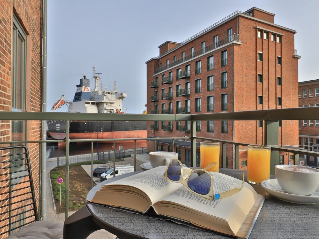 A balcony with a book, glasses, a bowl, and a glass of orange juice.