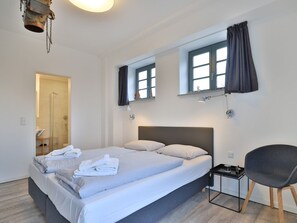 Une chambre d’hôtel moderne avec un grand lit, une petite table de chevet, une chaise et un espace douche.