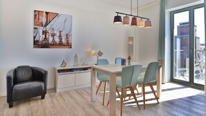 Et moderne spiseområde med et træbord og stole, en sort læderstol, et billede på væggen og udsigt gennem et stort vindue.