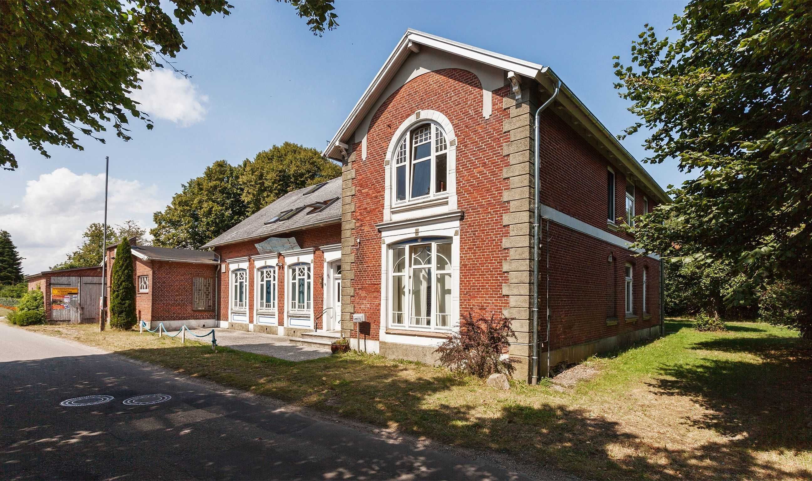 A red brick building with a gabled roof, large windows, and a small porch area.