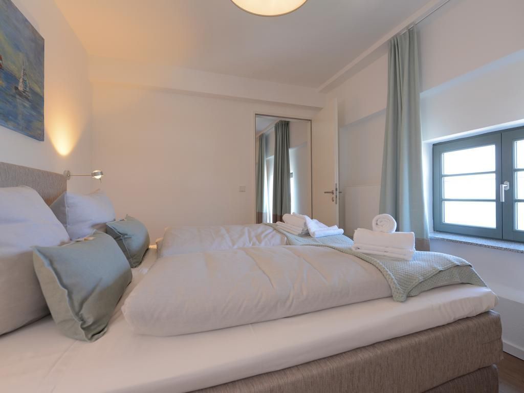 Una habitación de hotel moderna con una cama grande, una mesita de noche, un espejo y una ventana con cortinas.