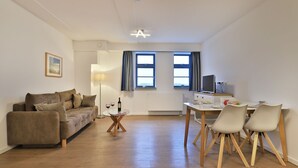 Un salon moderne comprenant un canapé, une table à manger avec des chaises, un téléviseur et une fenêtre avec des rideaux.