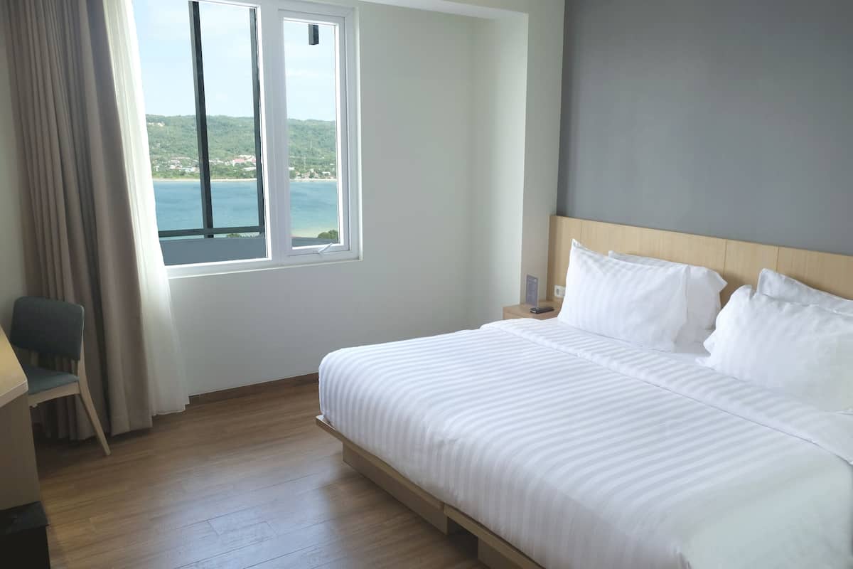 Hotellihuone, jossa on suuri sänky, työpöytä ja näköala merelle.