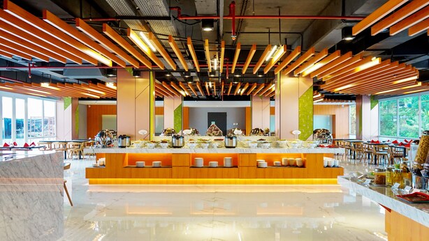 Een modern restaurant met een centraal eiland, houten balken in het plafond en grote ramen.