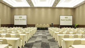 Een grote congrescentrum met rijen tafels en stoelen, twee banners voor Hotel Santika Ambon, en een vloerbedekking.