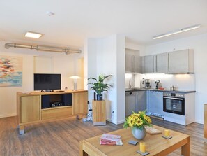 A modern living room with a wooden entertainment unit, a flat-screen TV, and a dining table with a vase of flowers.