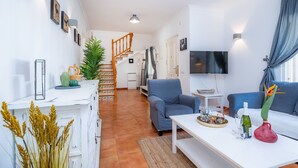 A modern living room with a staircase, a flat-screen TV, and a dining area with a table set for two.