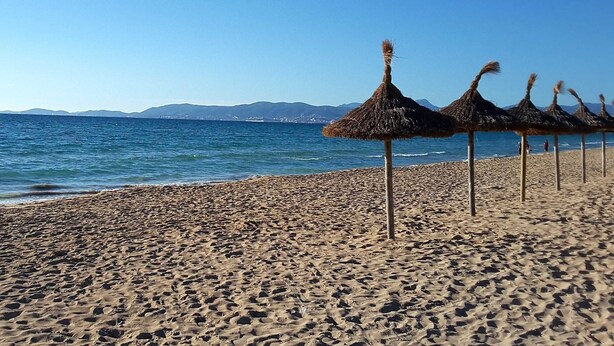 A beach with thatched umbrellas and a clear view of the sea and distant mountains.