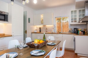 Une cuisine moderne avec des meubles blancs, une table à manger dressée avec des assiettes, des verres et un panier de fruits.