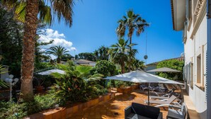 A sunlit patio with outdoor seating, palm trees, and a tiled floor.