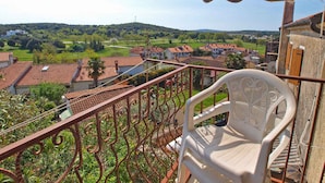 Un balcón con vistas a una zona residencial, una silla de plástico blanca y un toldo a rayas.