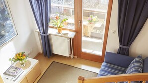 Un apartamento moderno con escalera de madera, un sofá azul, una mesita con una planta y vistas al exterior a través de un ventanal.
