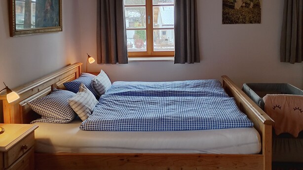 A bedroom with a bed, bedside tables, a window with curtains, and a painting on the wall. - Ferienwohnung Nr 1,  2 Pers. 50 qm (Schleching)
