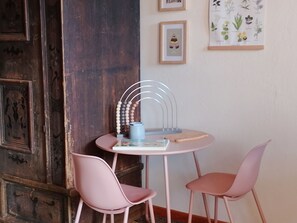 A small round table with two pink chairs, a wooden door, and framed botanical prints on the wall.