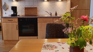 A kitchen with wooden cabinets, a coffee maker, a sink, and a vase with flowers on the table. - Ferienwohnung Nr 1,  2 Pers. 50 qm (Schleching)