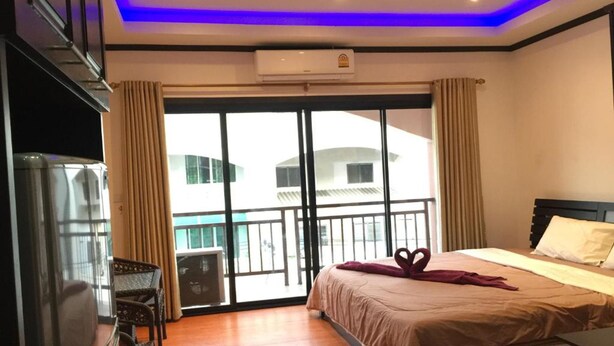A hotel room with a bed, a TV, a balcony with curtains, and an air conditioning unit. - K&J Apartment (Pattaya)