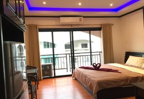 A hotel room with a bed, a TV, a balcony with curtains, and an air conditioning unit. - K&J Apartment (Pattaya)