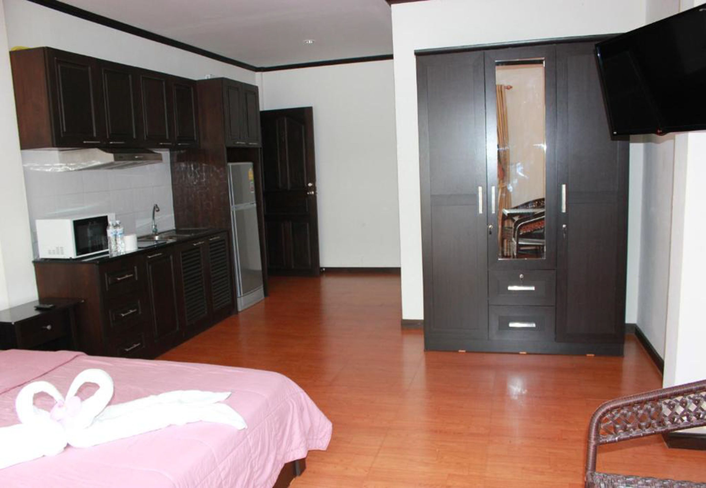 A bedroom with a bed, a wardrobe, a television, and a kitchenette.