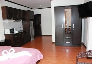 A bedroom with a bed, a wardrobe, a television, and a kitchenette. - K&J Apartment (Pattaya)
