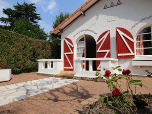 Ein Gebäude mit roten Fensterläden, weißem Zierdekor und einem Steinweg, der zum Eingang führt.