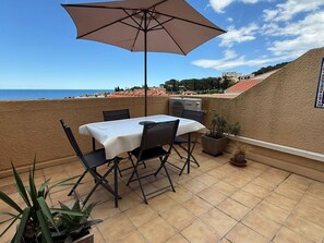 Eine Terrasse mit Tisch, Stühlen und Sonnenschirm, mit Blick aufs Meer.