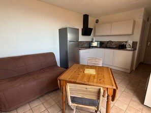 Una cocina funcional con refrigerador, microondas y cafetera. Hay una mesa de madera con un banco, un sofá marrón y gabinetes blancos.