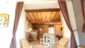 Una habitación acogedora con techo de madera, sillas de mimbre, una mesa con cojín y una escalera que sube a otra zona.