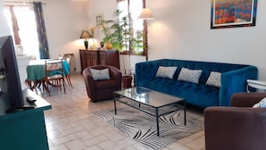 A living room with a blue sofa, a brown armchair, a glass coffee table, and a dining area with a table and chairs. - Quiet cottage near Azay-le-Rideau Castle (Azay-le-Rideau)