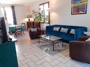 Un salon avec un canapé bleu, un fauteuil marron, une table basse en verre et un coin repas comprenant une table et des chaises.